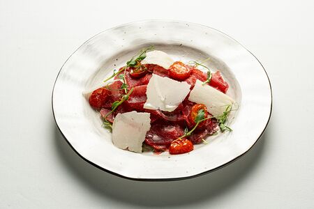 Карпаччо из говядины с запеченными помидорами, сыром грана подано и рукколой