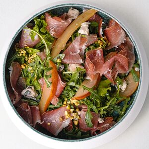 Салат с руколой, пармским окороком, томлёной грушей, горгонзолой и солёной фисташкой