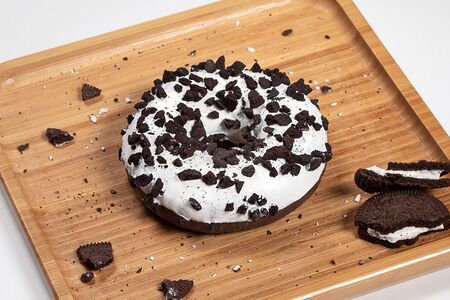 Пончик-донат с белой начинкой, белой кондитерской глазурью с кусочками печенья Cookies